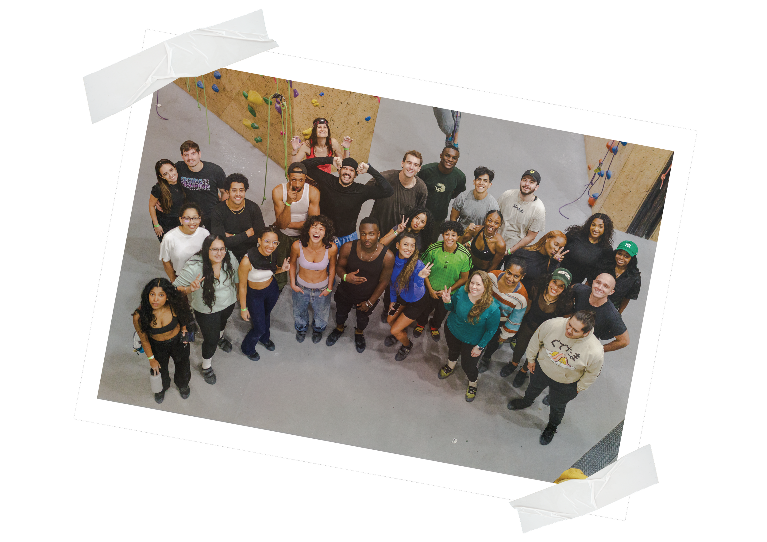 Group of young adults posing for a photo at an indoor rock climbing gym, with climbing walls in the background.
