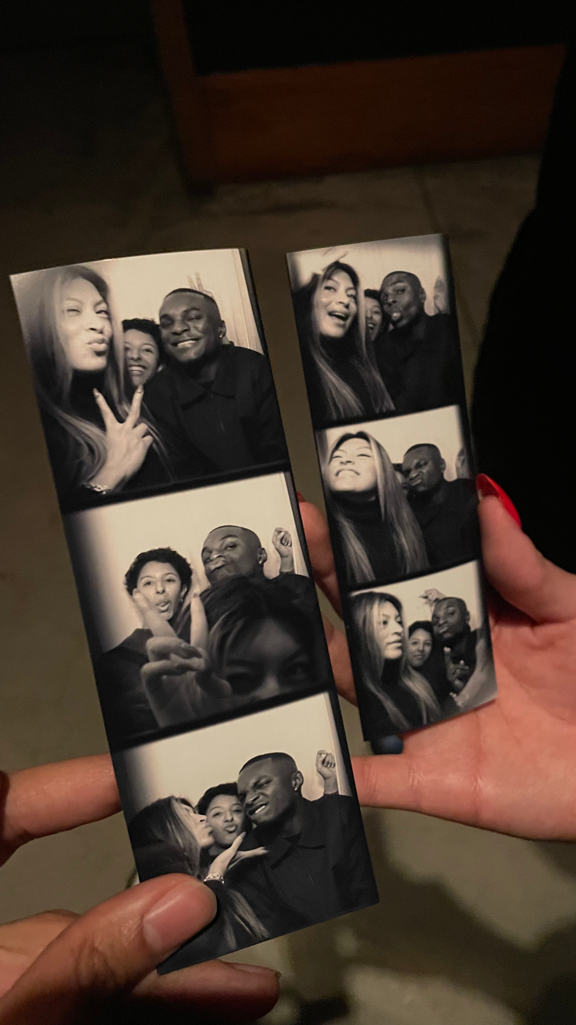 Two people holding photo booth strips with black and white photos of a group of friends making funny faces and poses.
