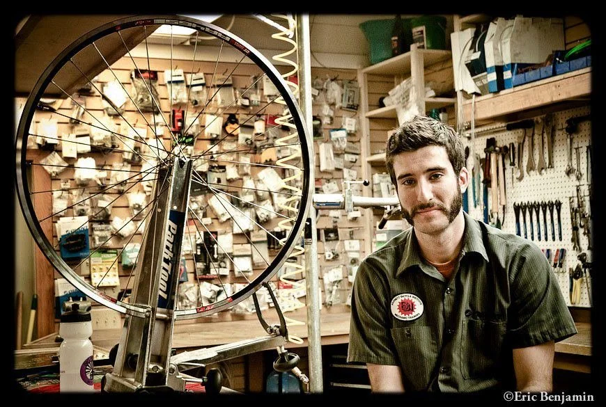 Aaron Apel, bicycle mechanic sitting in a repair shop.