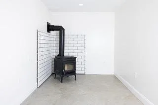 Empty room with a wood stove in the corner, surrounded by white brick tiles and plain white walls.