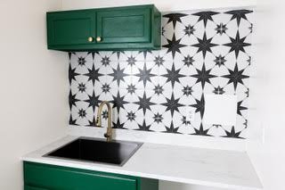 Kitchen with green upper cabinet, black sink, white countertop, and black and white star-patterned backsplash