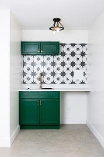 Small kitchen area with green cabinets, a gold-colored faucet, a white countertop, and a decorative black and white starburst patterned tile backsplash.