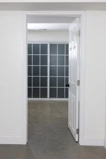View through a doorway into a room with large grid-style window panels and beige carpet.
