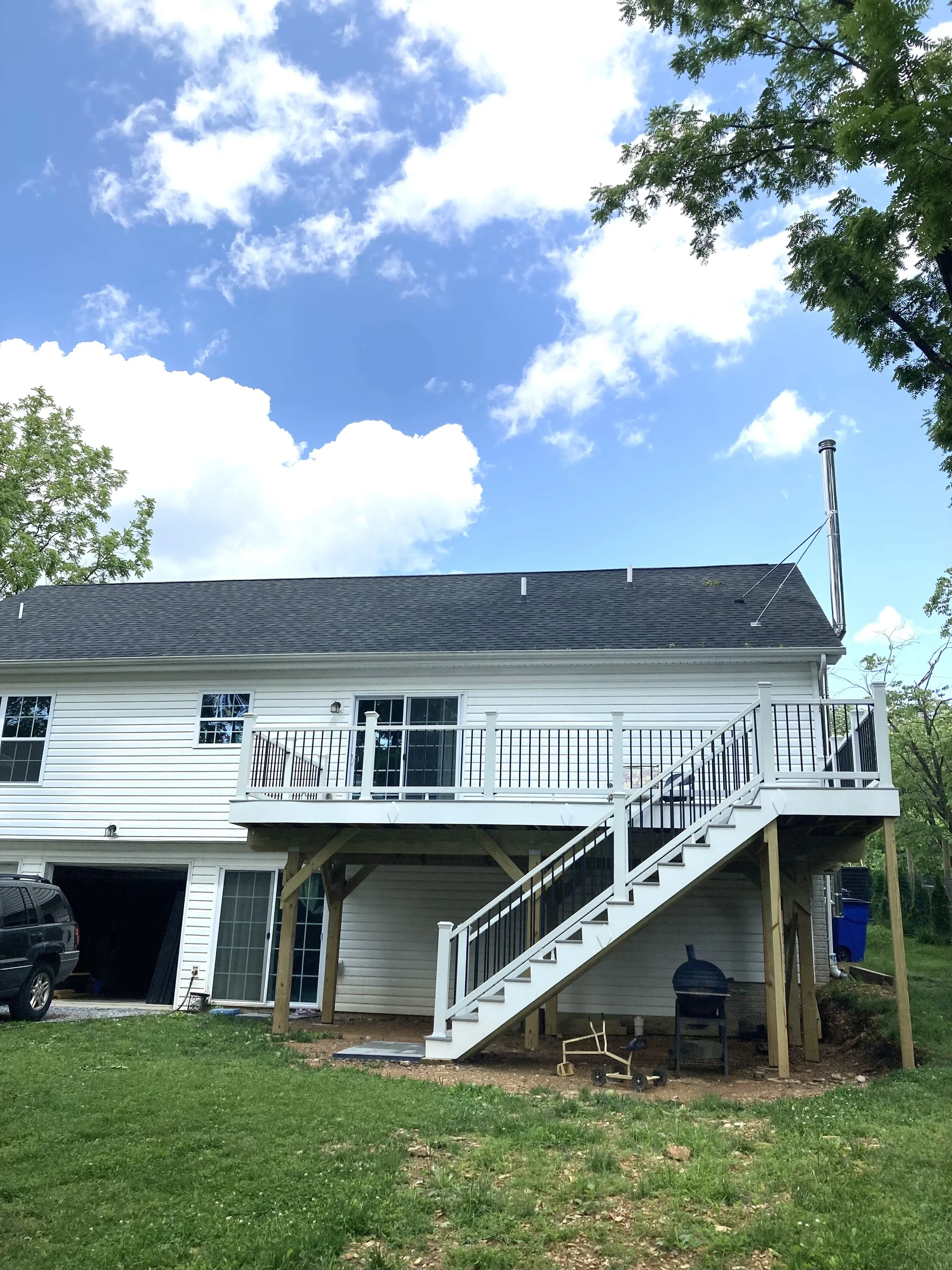 Backyard view of a white house with an elevated deck and staircase, with a blue sky and clouds overhead.