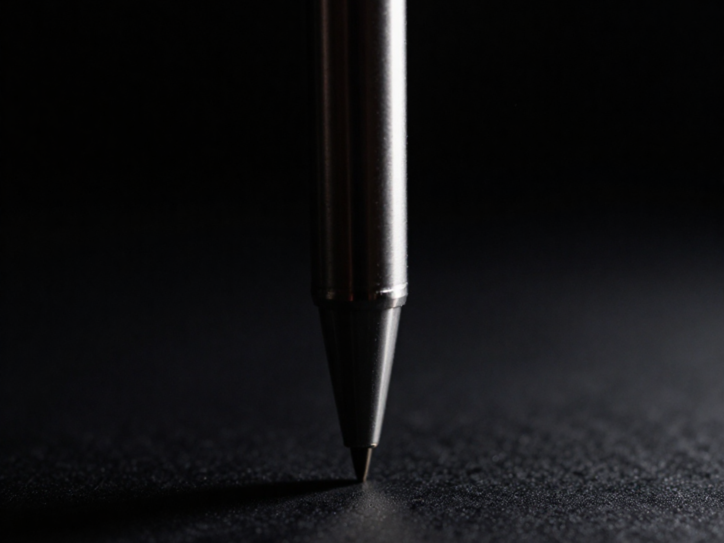 Close-up of a metallic ballpoint pen tip touching a dark textured surface.