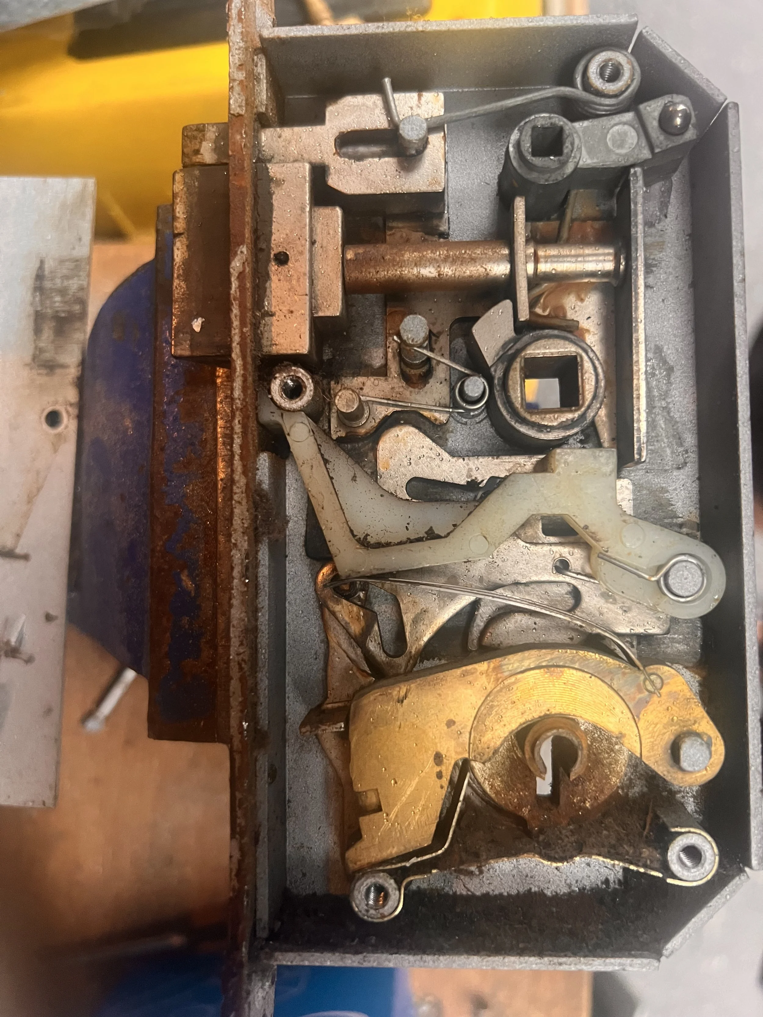 Close-up view of a mechanical lock mechanism with various metal components, levers, and a brass-colored lock cylinder, mounted inside a metal housing.