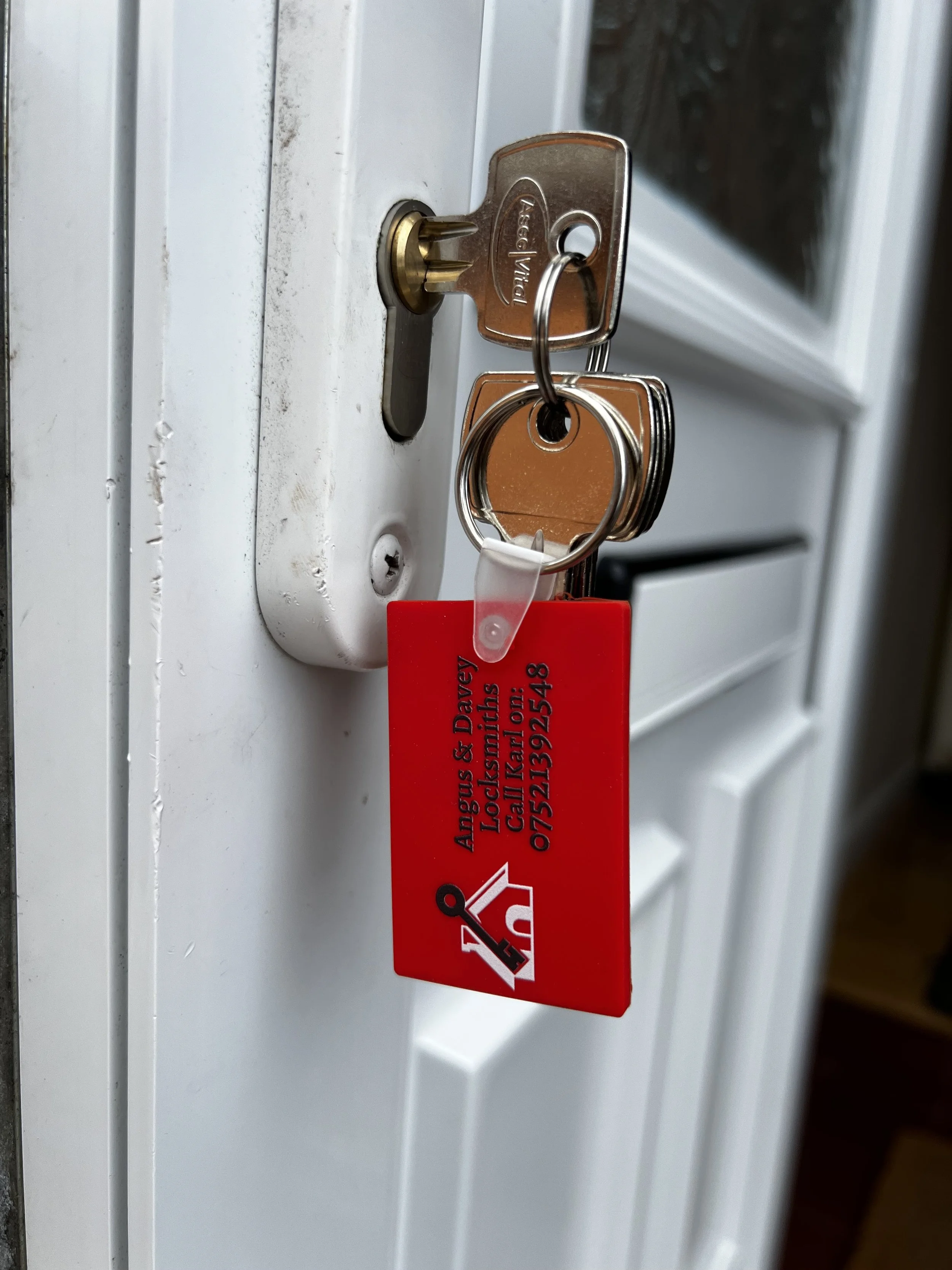 A close-up photo of a door lock with a key inserted, attached to a set of keys and a red key tag with contact information.