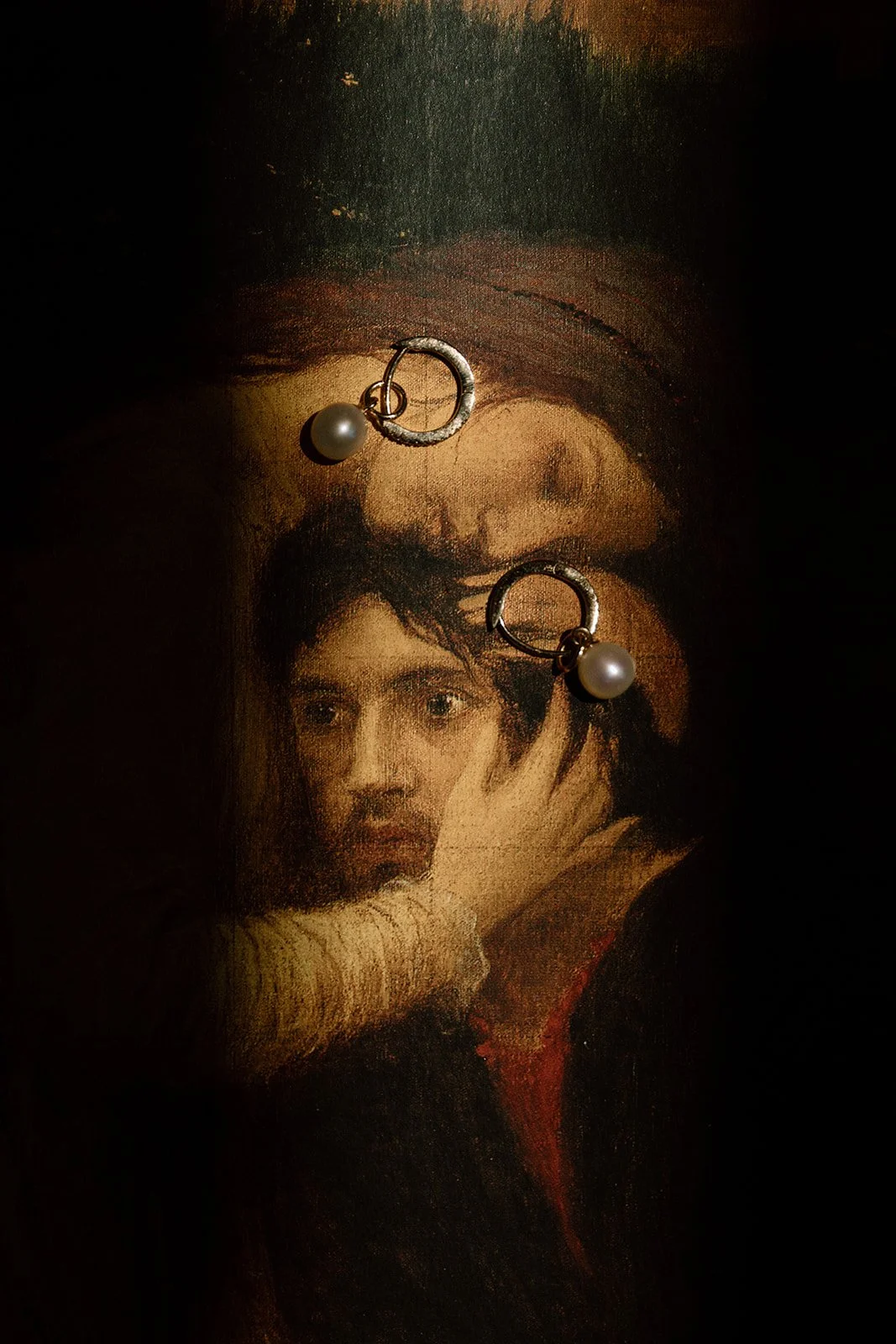 Pearl earrings placed on a painting of a woman with dark hair, looking directly at the viewer, with her hand resting on her face.