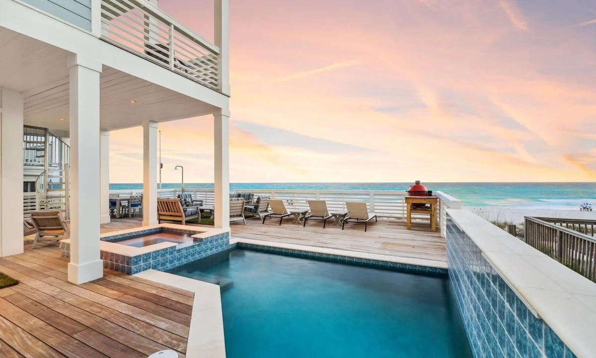 Luxury seaside vacation home featuring a private pool, outdoor lounge area, ocean view, and sunset sky.