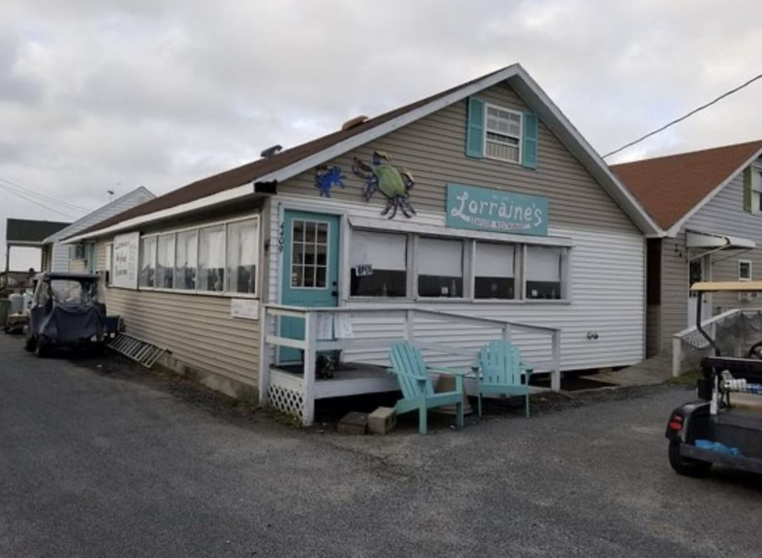Exterior view of Lorraine's, a small eatery with a sign, featuring a porch with two turquoise Adirondack chairs, a door, and a mural of cartoon insects painted on the building.