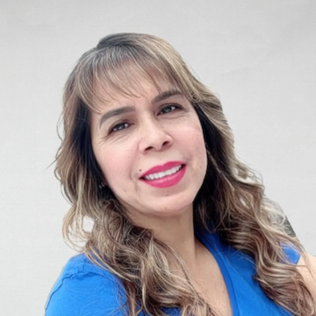 A woman with shoulder-length wavy light brown hair and light skin, smiling, wearing pink lipstick and a bright blue top.
