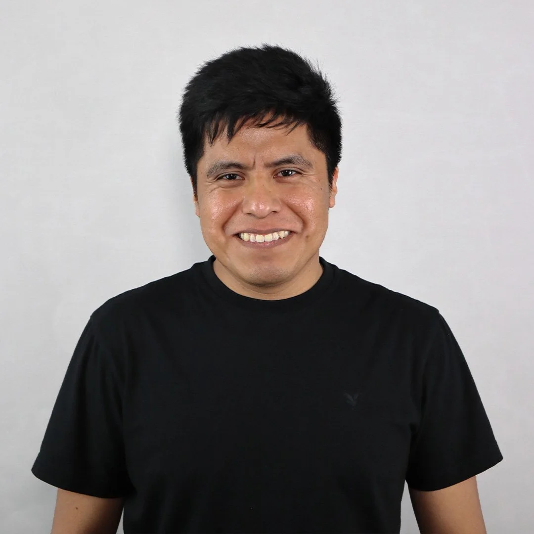A smiling man with short black hair wearing a black t-shirt standing against a plain white background.