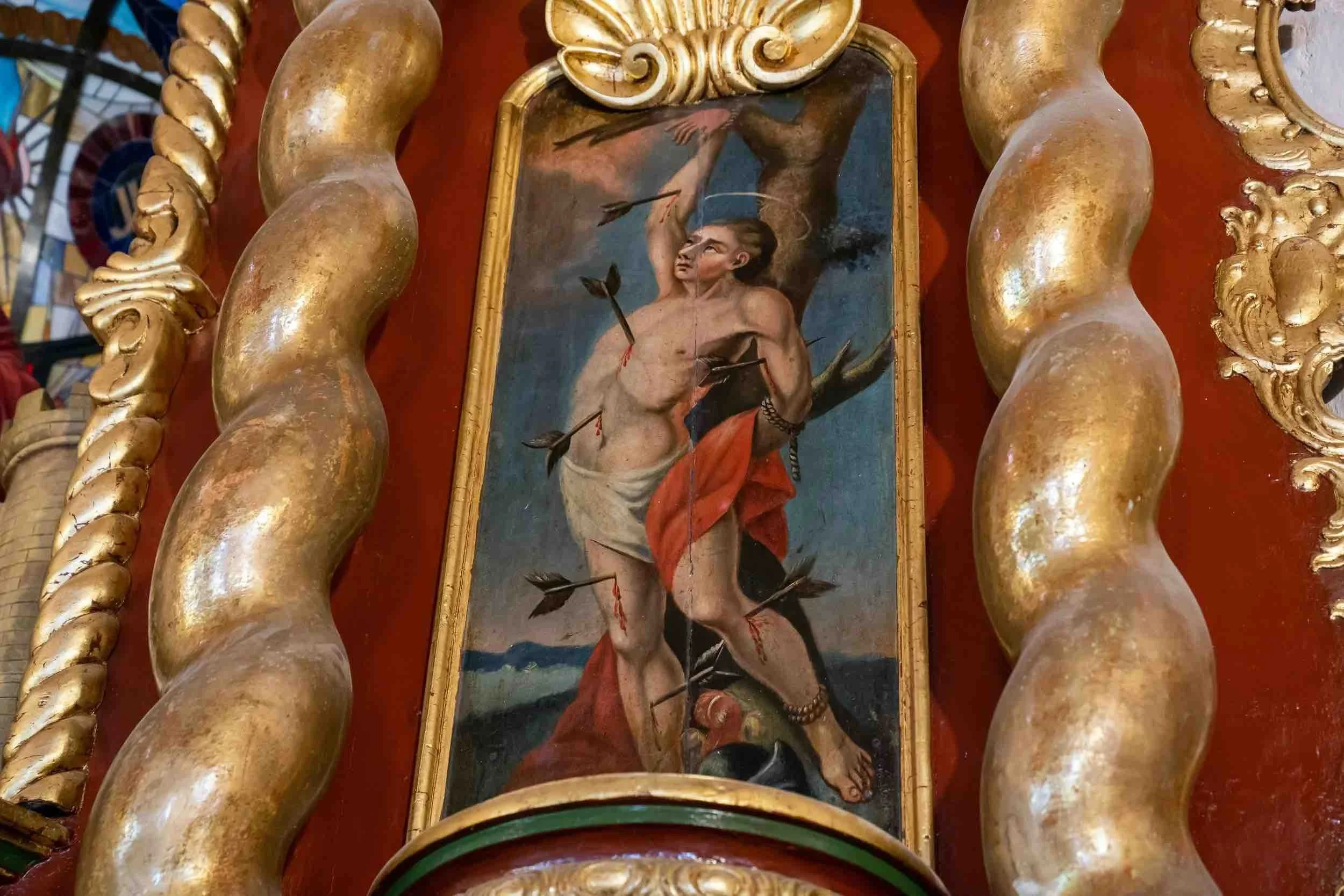 A religious painting depicting Saint Sebastian tied to a post, shot with arrows, with a golden ornate frame.