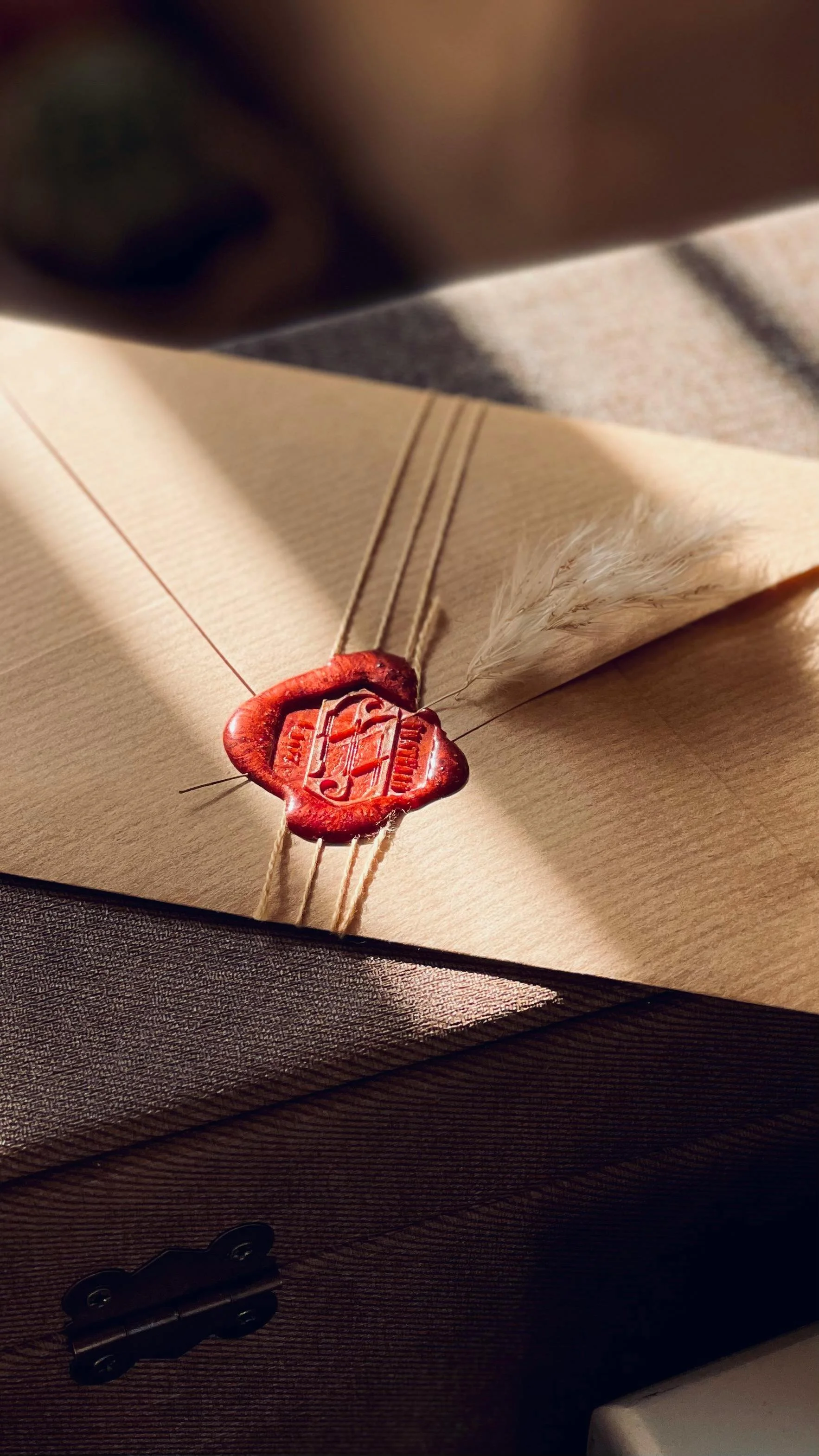 A beige envelope sealed with red wax and tied with string, with a feather tucked under the string.