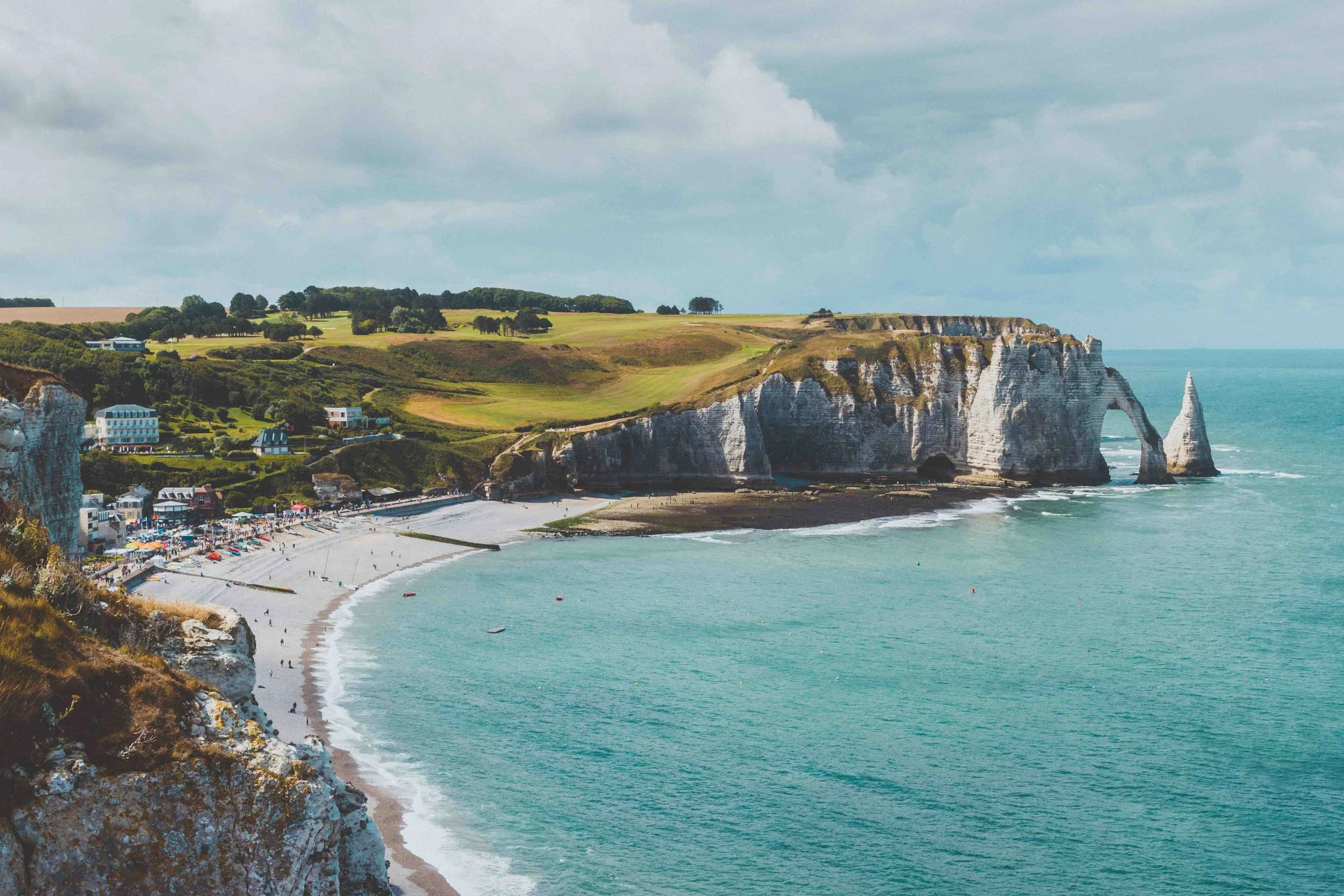 Scenic view of Normandy cliffs and beach, with white chalk cliffs, green hills, and the ocean, under a partly cloudy sky.