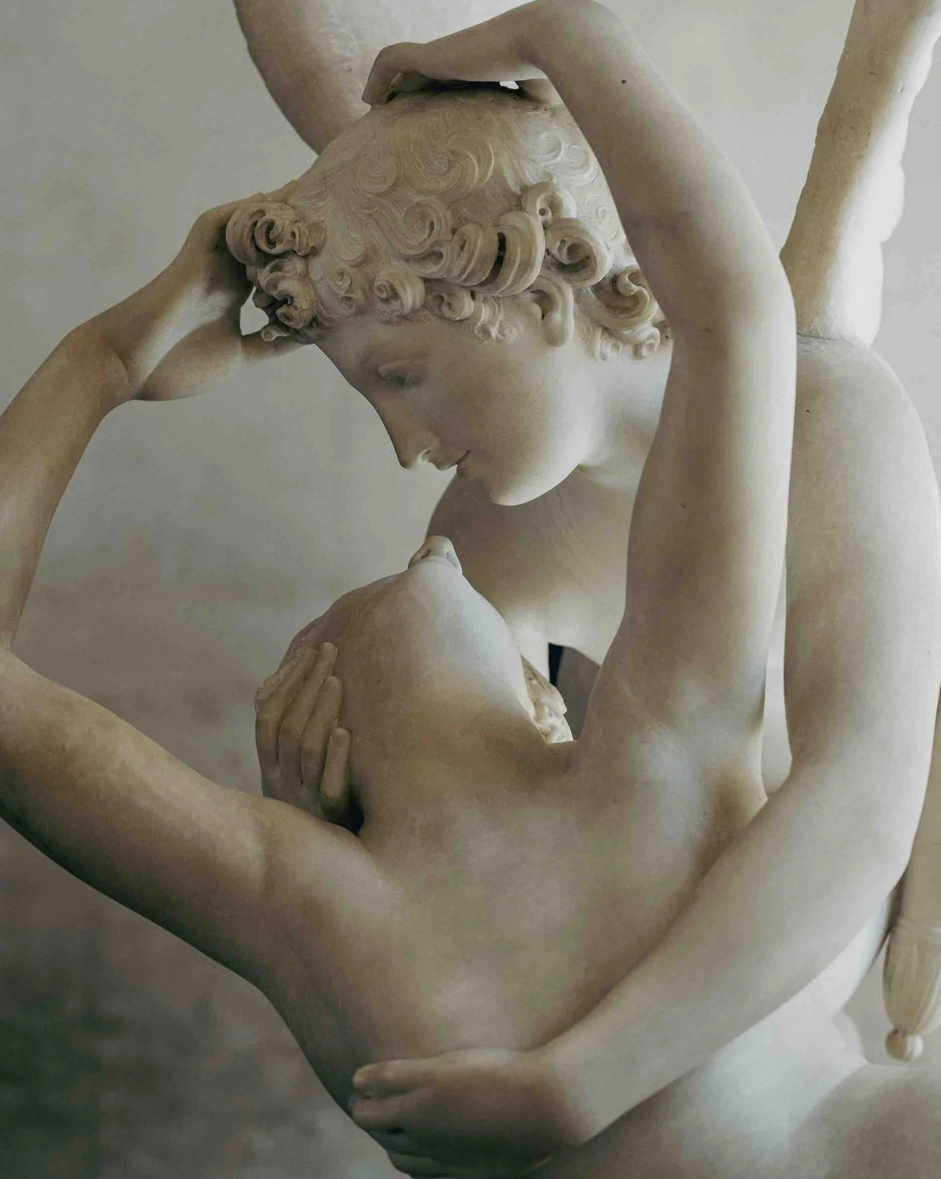 Close-up of a classical marble sculpture depicting a woman with curly hair, touching her forehead with one hand and holding a baby with the other, both with gentle expressions.