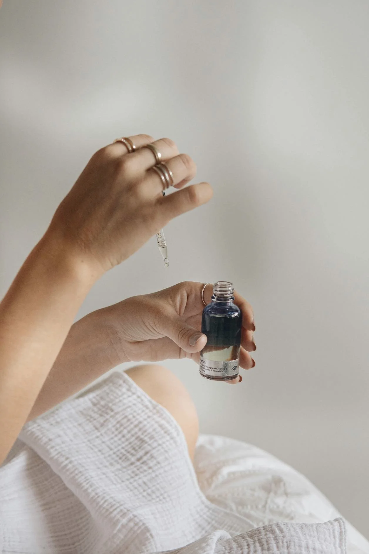 Person drawing liquid from a small dropper bottle into a larger bottle of liquid.