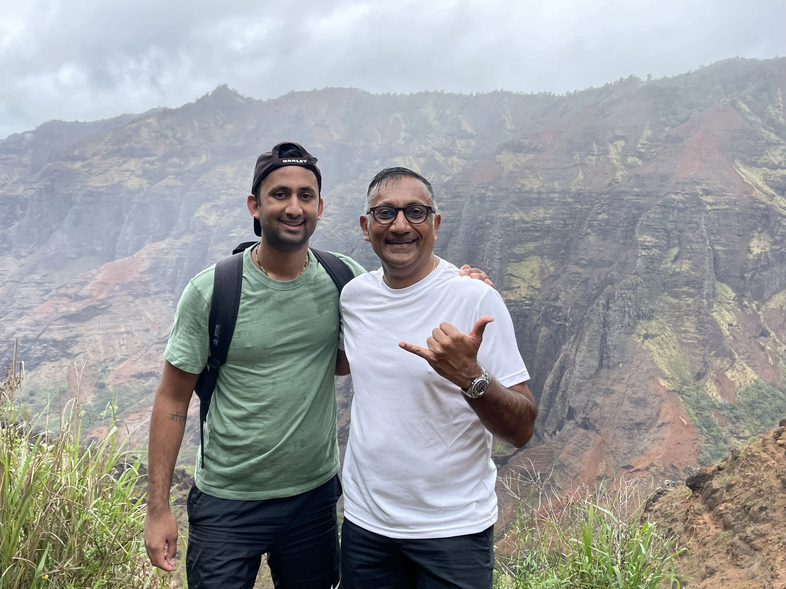 Two men standing side by side outdoors with mountains in the background, smiling at the camera.