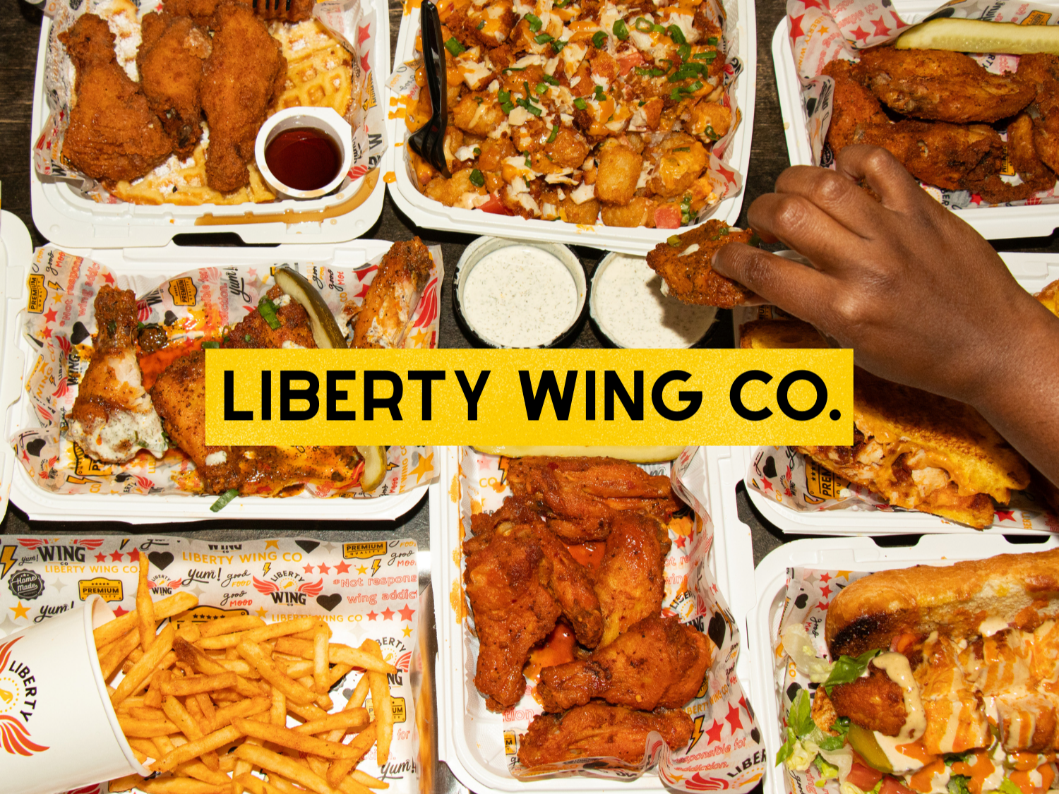 An assortment of fried chicken, French fries, and various loaded baked goods in takeout containers from Liberty Wing Co.