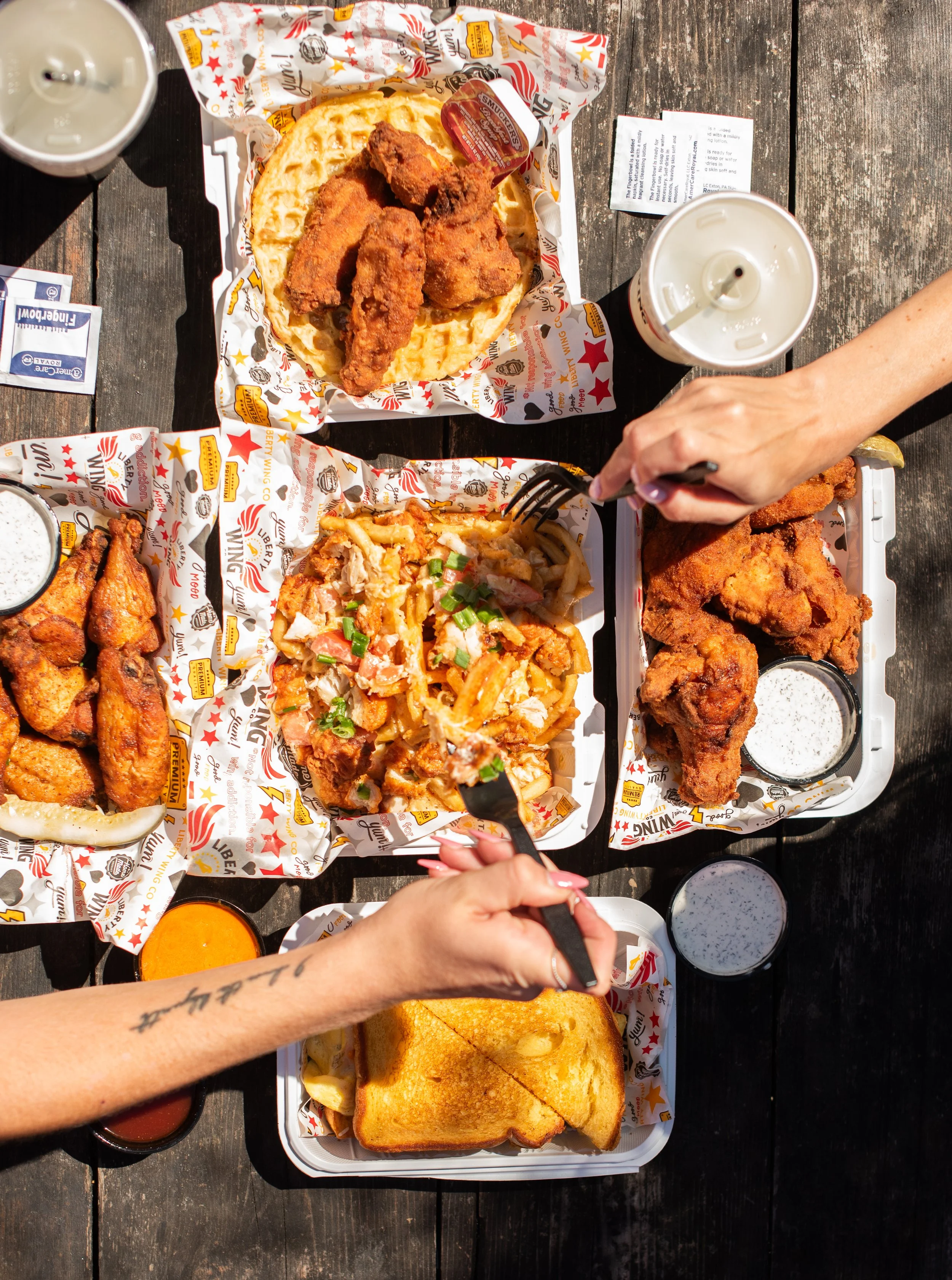 Overhead view of a table with various Southern-style American foods including fried chicken wings, fried fish fillets, chicken and fries nachos topped with green onions, and a grilled cheese sandwich, along with drinks and condiments.
