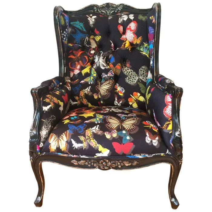 Vintage armchair with black wooden frame and floral-patterned upholstery covered in vibrant butterfly prints.