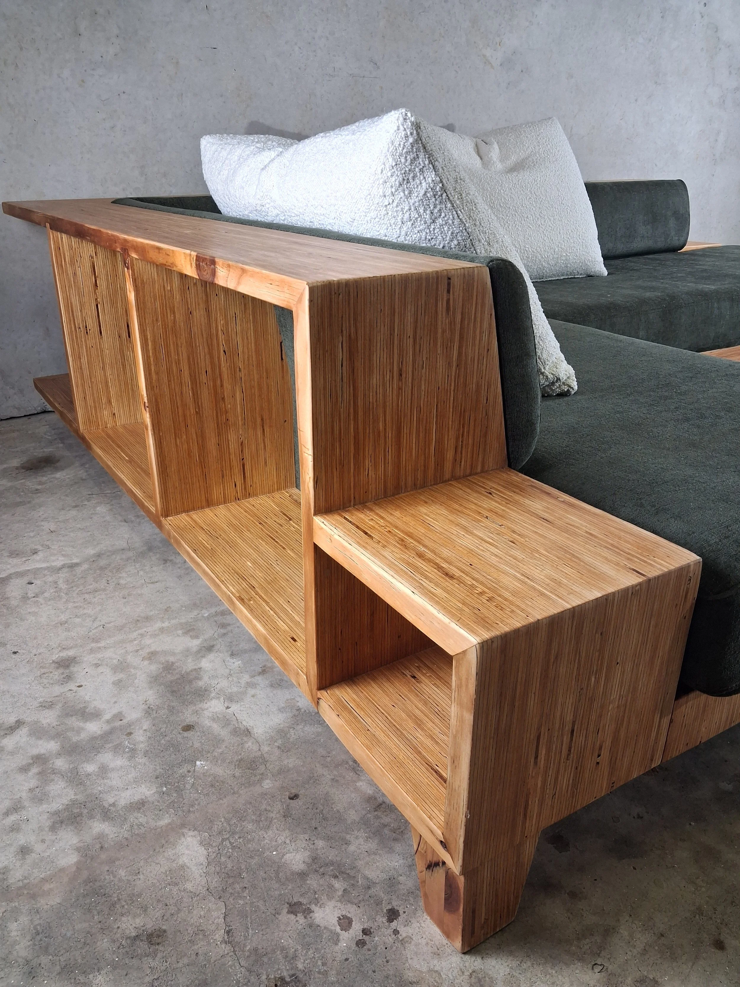Wooden modular shelf unit with open cubbies next to a dark upholstered sofa with white textured pillows, in a room with concrete floor and wall.