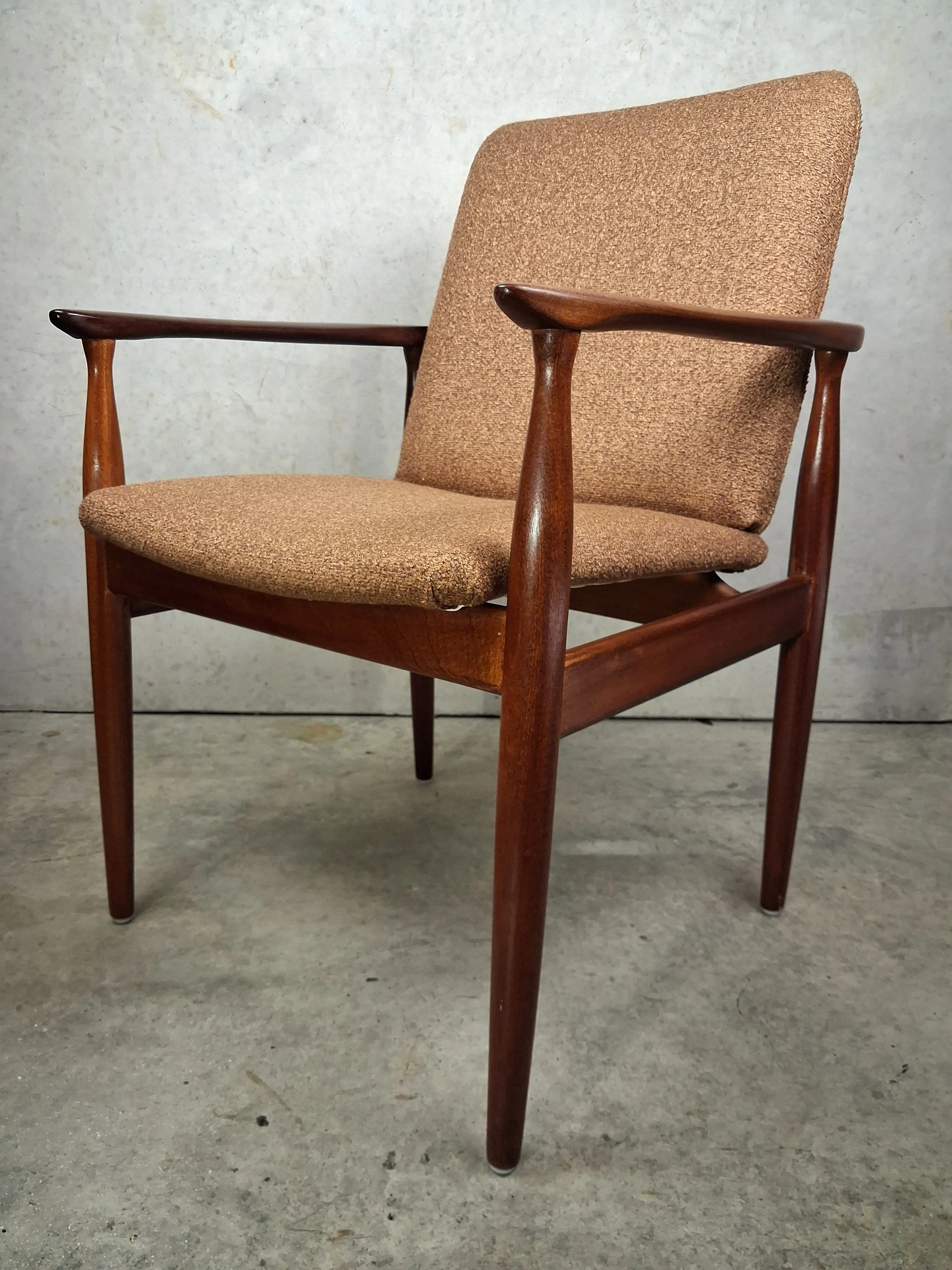 Mid-century modern armchair with wooden frame, beige fabric upholstery on the seat and backrest, set against a concrete background.