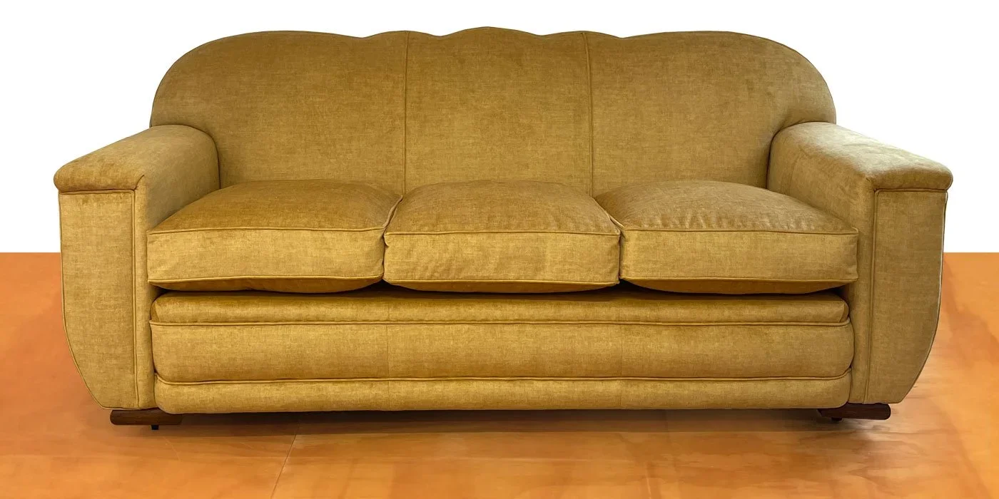 A mustard yellow sofa with three cushions on a wooden floor.