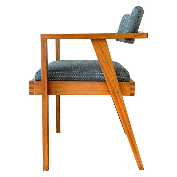 Side view of a wooden chair with a padded blue cushion on the seat and backrest, featuring angled legs.