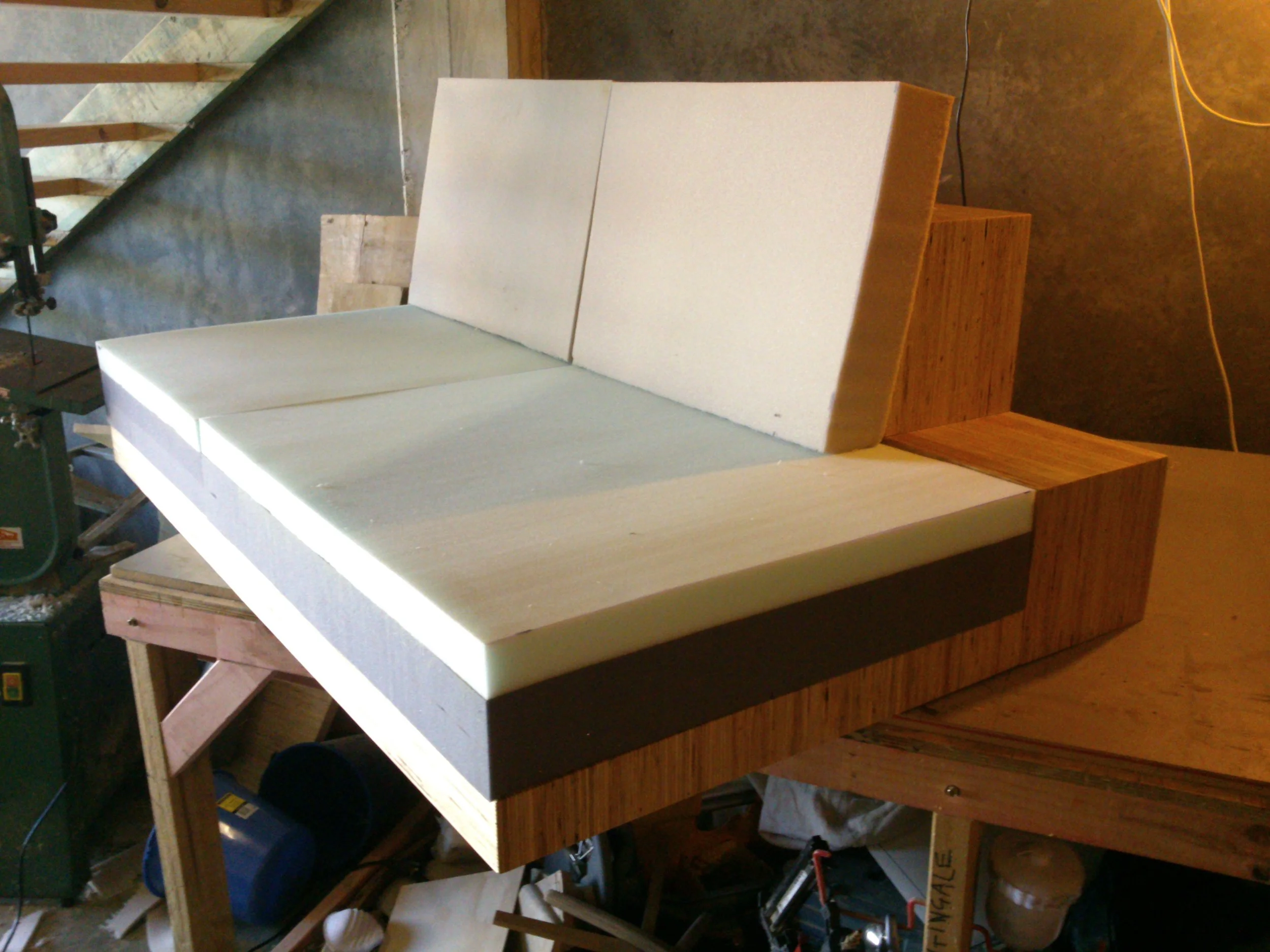 A wooden and foam sculpture resembling a modern sofa in a workshop.