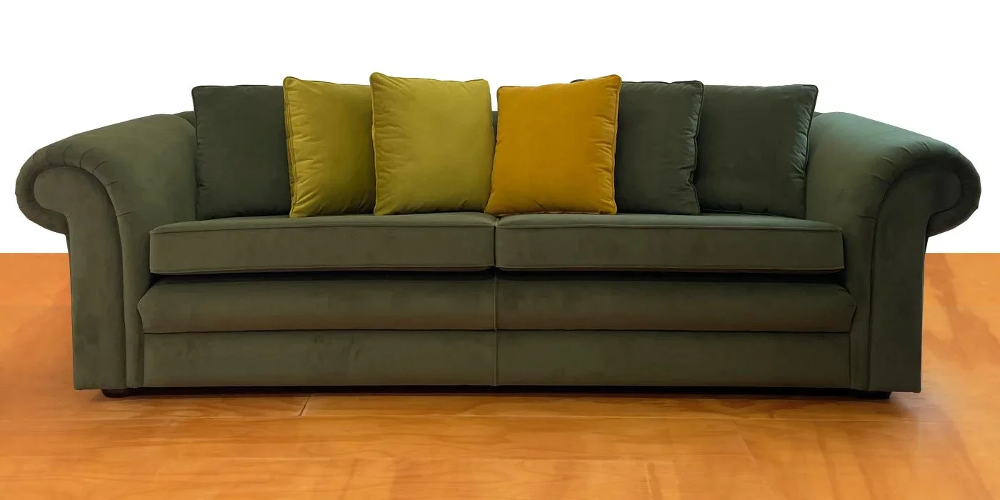 Dark green sofa with five pillows in shades of yellow and green, placed on a wooden floor against a plain white background.