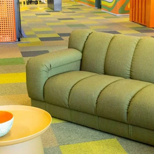 A green upholstered sofa in a colorful, modern indoor space with a patterned carpet and a small round table nearby.