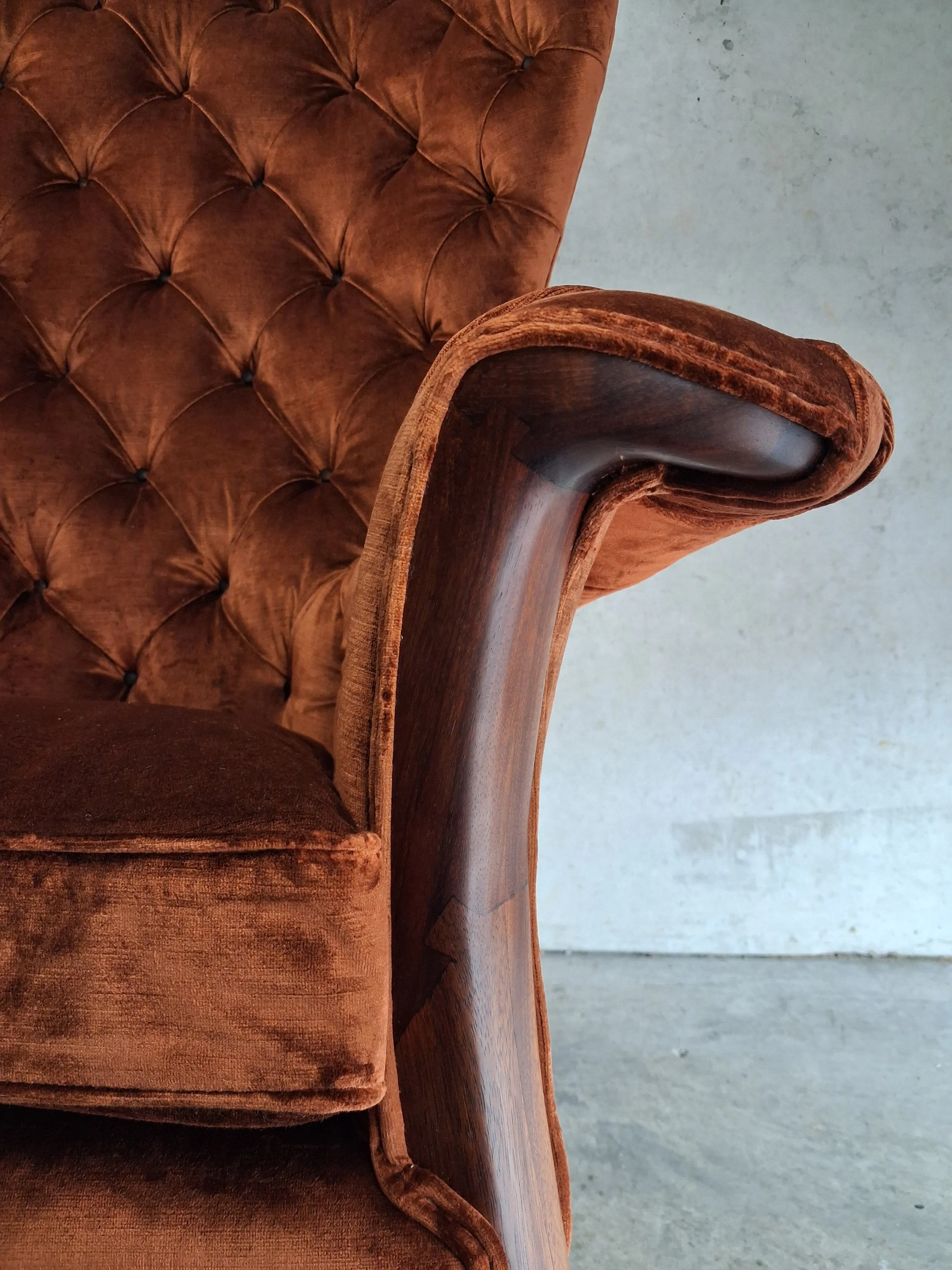 Close-up of a custom brown velvet armchair with tufted backrest and wooden armrest and frame.