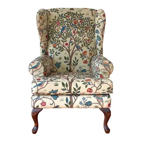 Upholstered wingback armchair with a floral and bird pattern fabric, wooden curved legs, and rolled armrests.