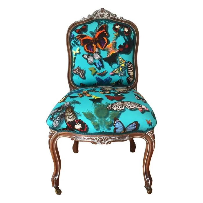 An ornate wooden chair upholstered with fabric featuring colorful butterfly patterns on a turquoise background.