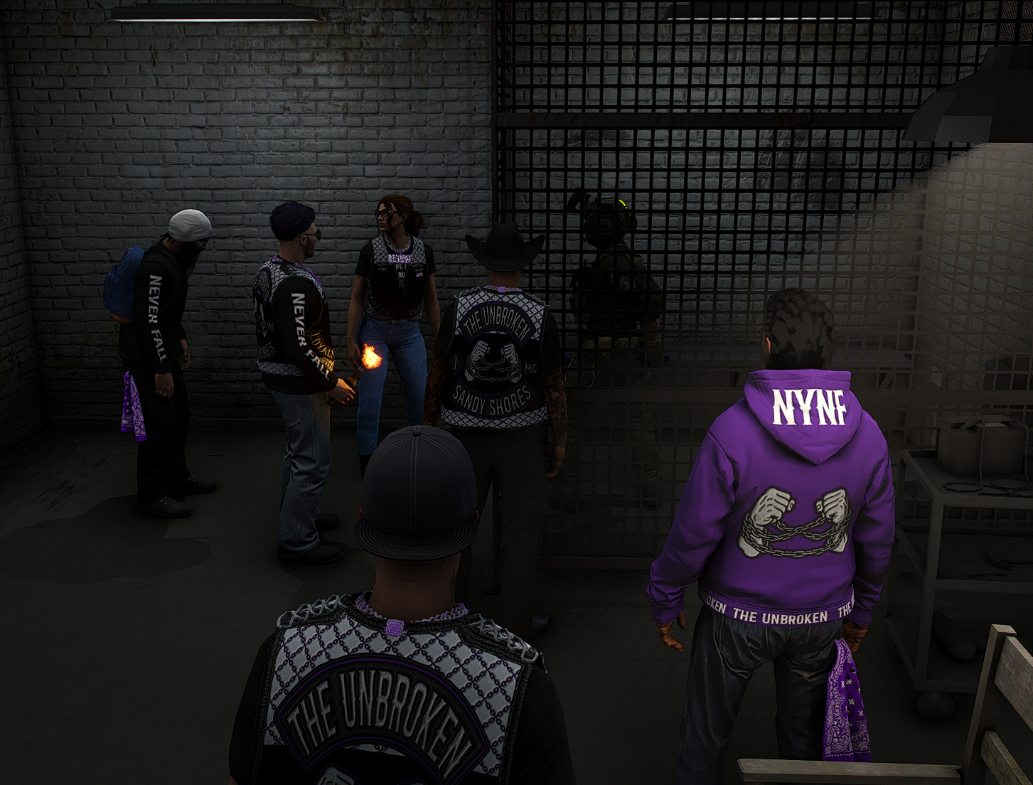A group of seven people, five men and two women, gathered in a dimly lit room with gray brick walls and a cell-like environment. They are wearing clothing with patches, patches reading "The Unbroken," and purple bandanas. One person holds a lit flare. Two people are behind a metal bars dividing the space, with one sitting and the other standing.