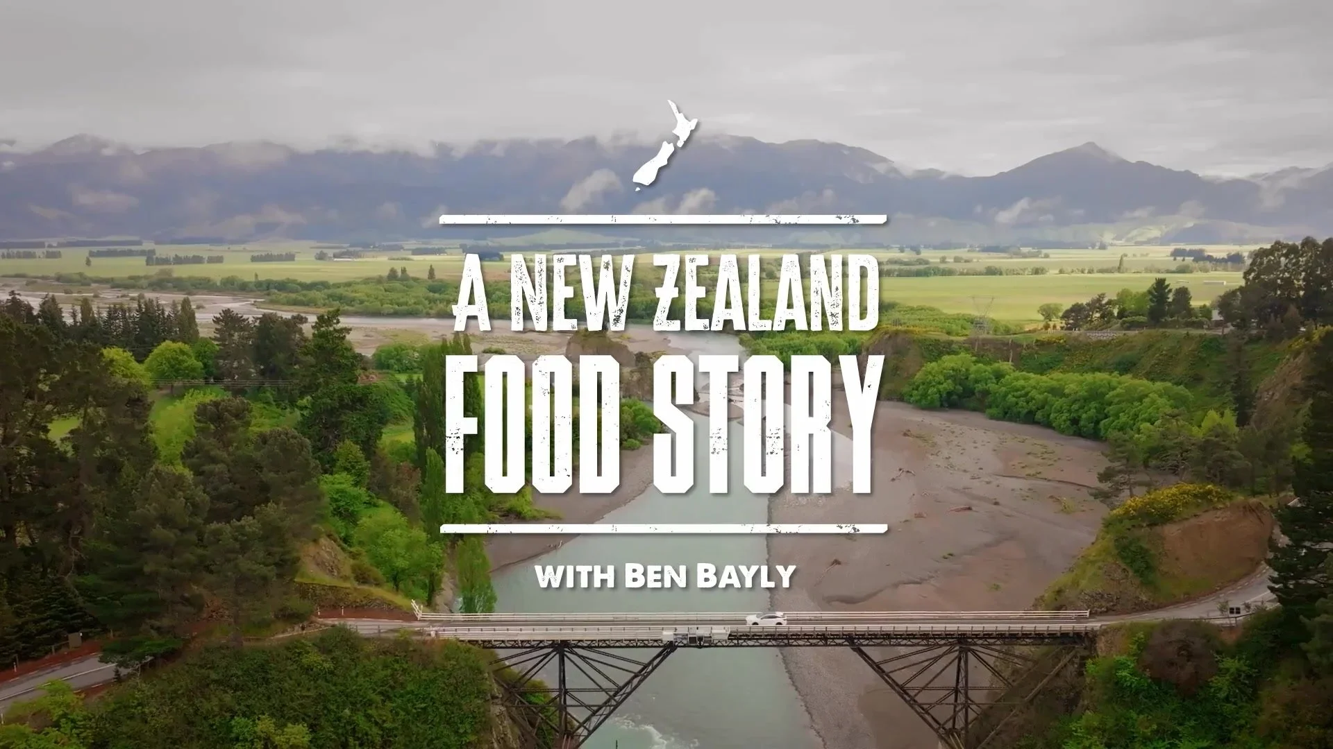 A scenic landscape of New Zealand with a river running through lush green trees and hills, and mountains in the background under a cloudy sky. Overlaid text reads 'A New Zealand Food Story with Ben Bayly'.