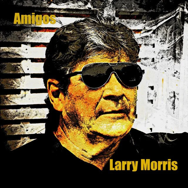 A man wearing dark sunglasses, with gray hair, against a striped background. The text says "Amigos" and "Larry Morris" in yellow.