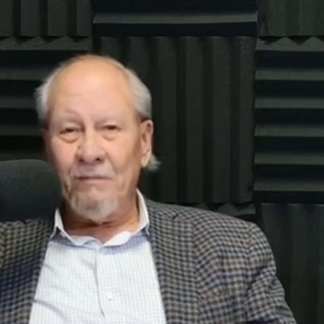 Older man with gray hair and beard sitting in a recording studio with soundproof foam panels.