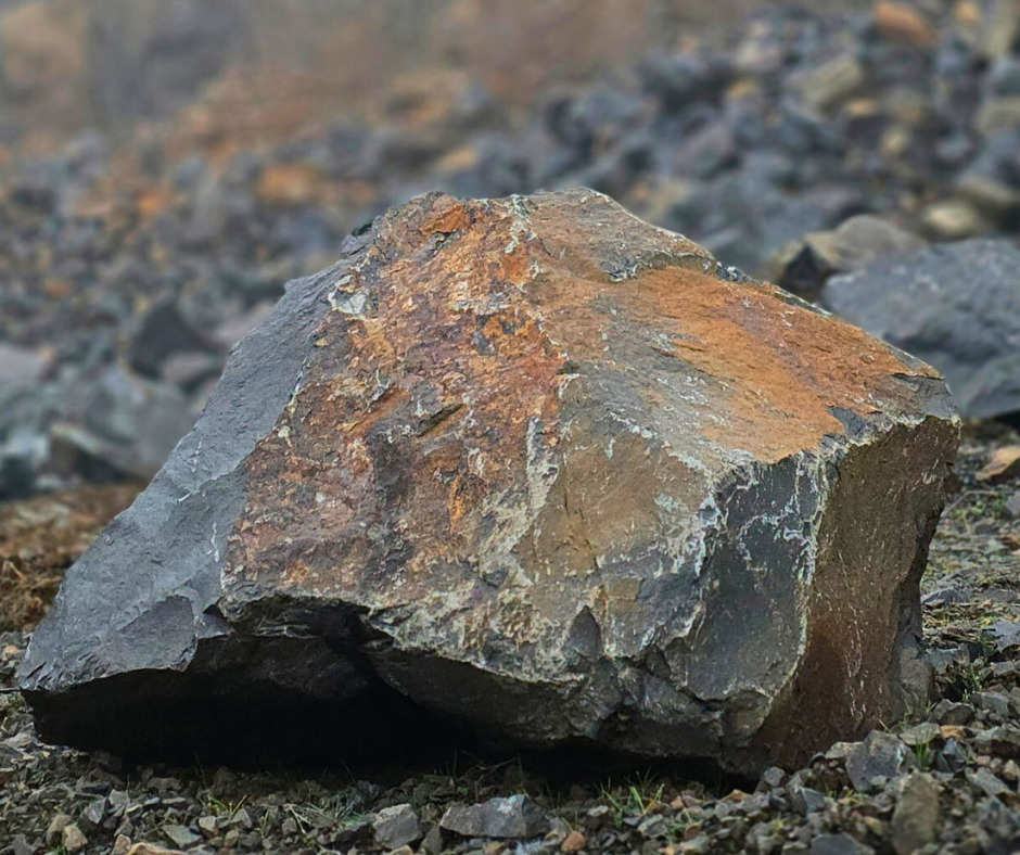 A large, rough, gray and brown rock on a gravelly ground also known as as riprap boulders. These landscaping rocks can be picked-up at Bedrock Holdings Group's Haley Heritage location in Sweet Home, Oregon.