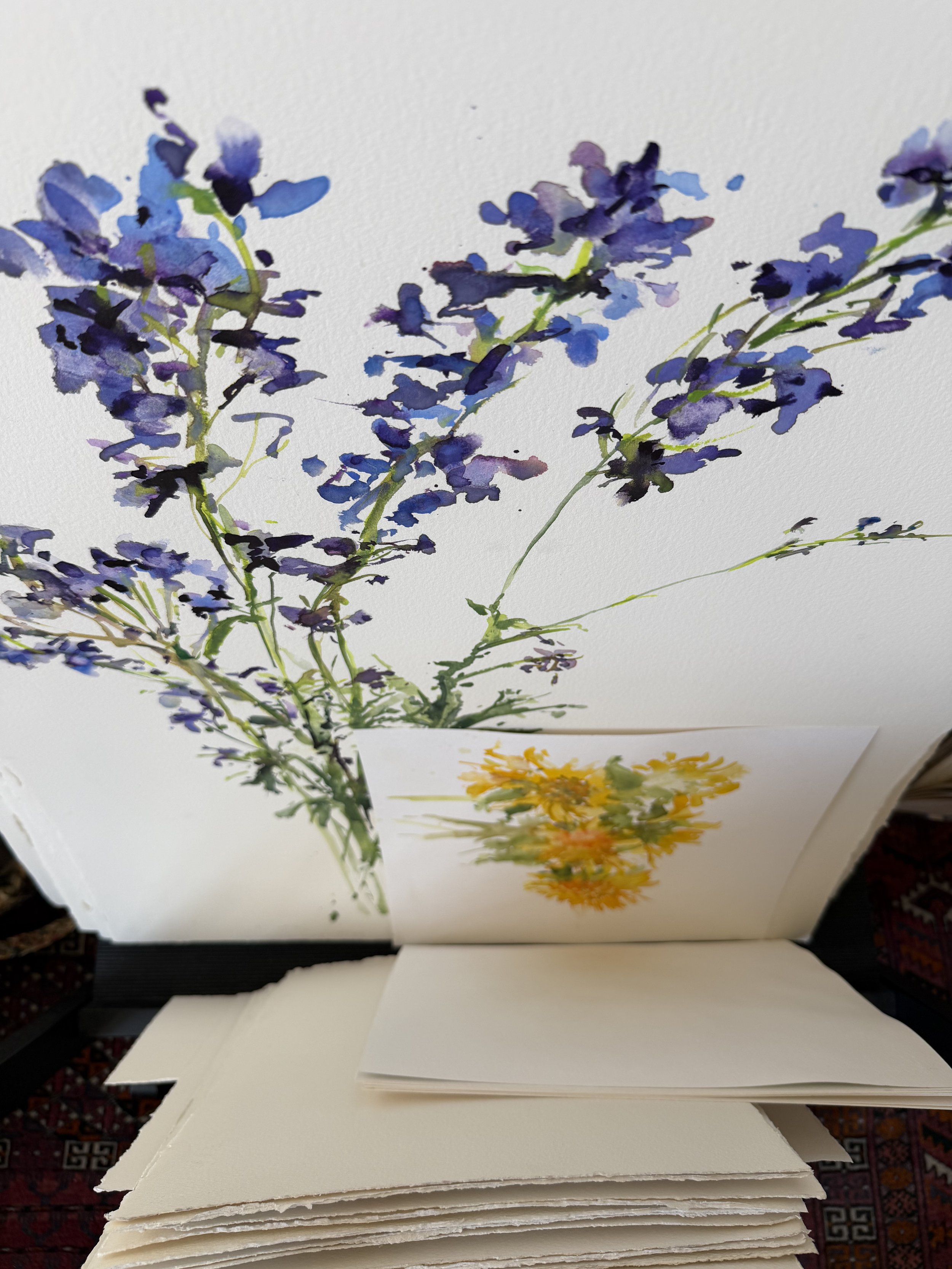 Watercolor painting of purple flowers on a white background, with another painting of yellow flowers below.
