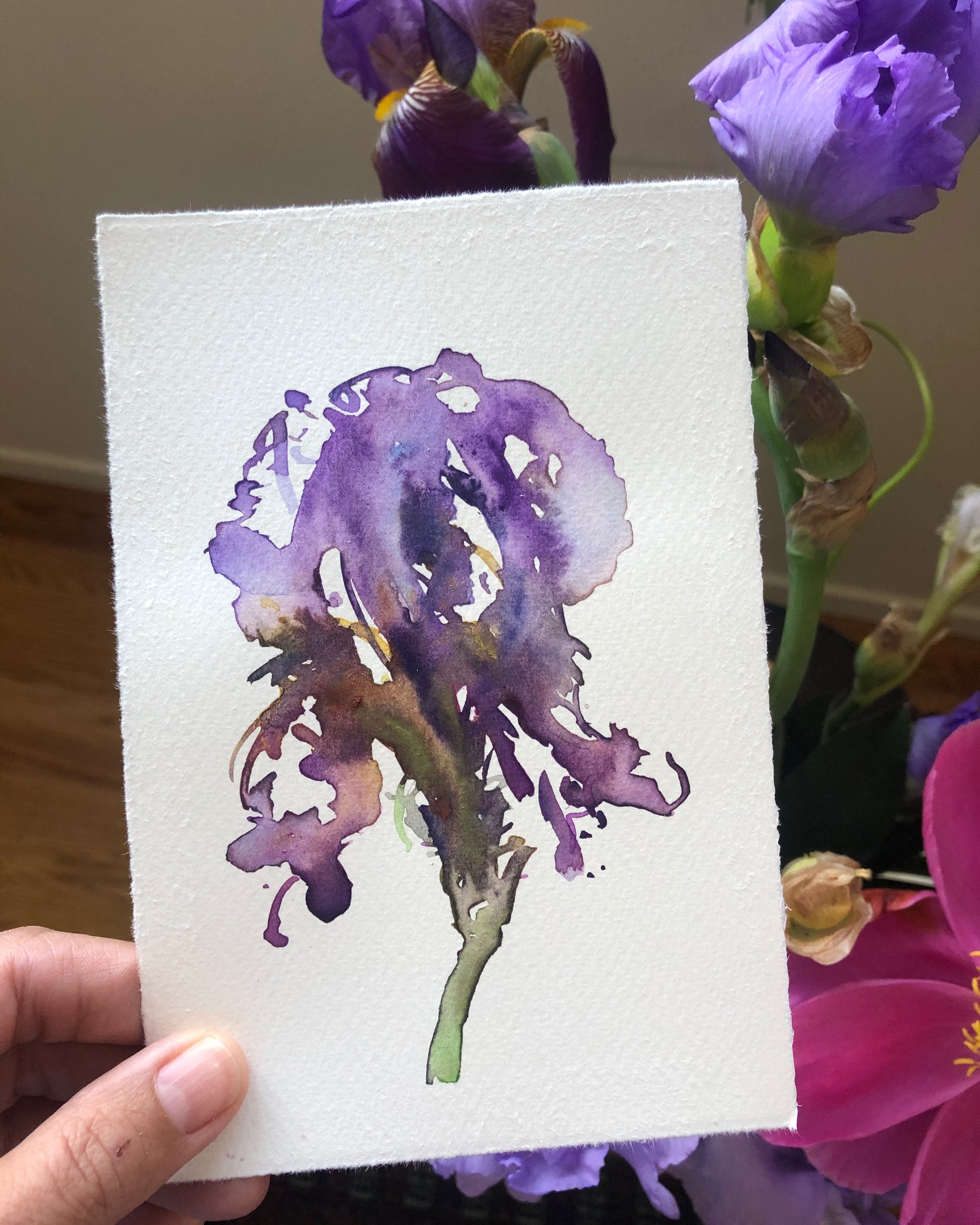 A watercolor painting of a purple iris flower on textured white paper, with purple and pink irises in the background.