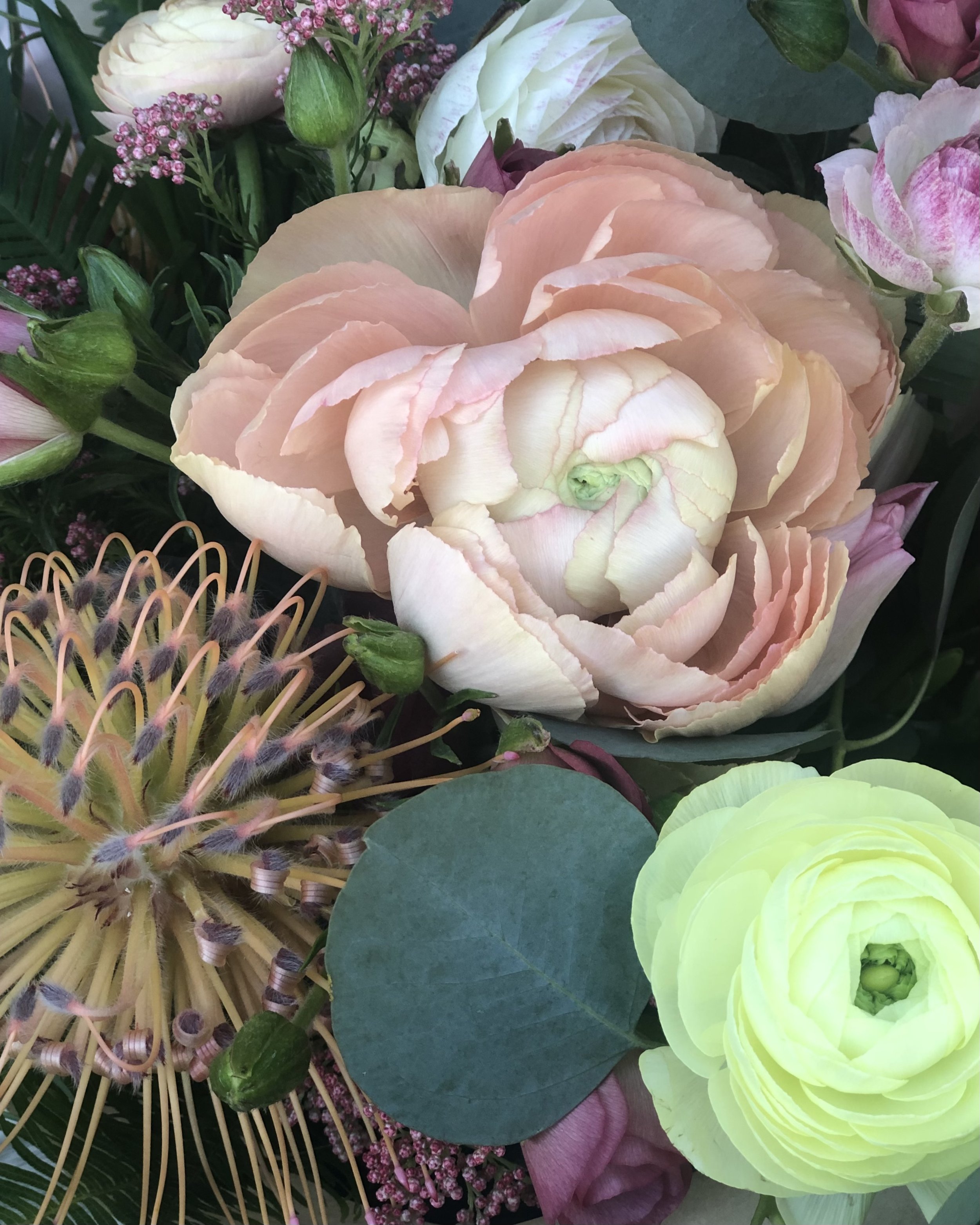 Close-up of a bouquet of flowers with pink, white, and yellow blossoms, including large peonies and other greenery.