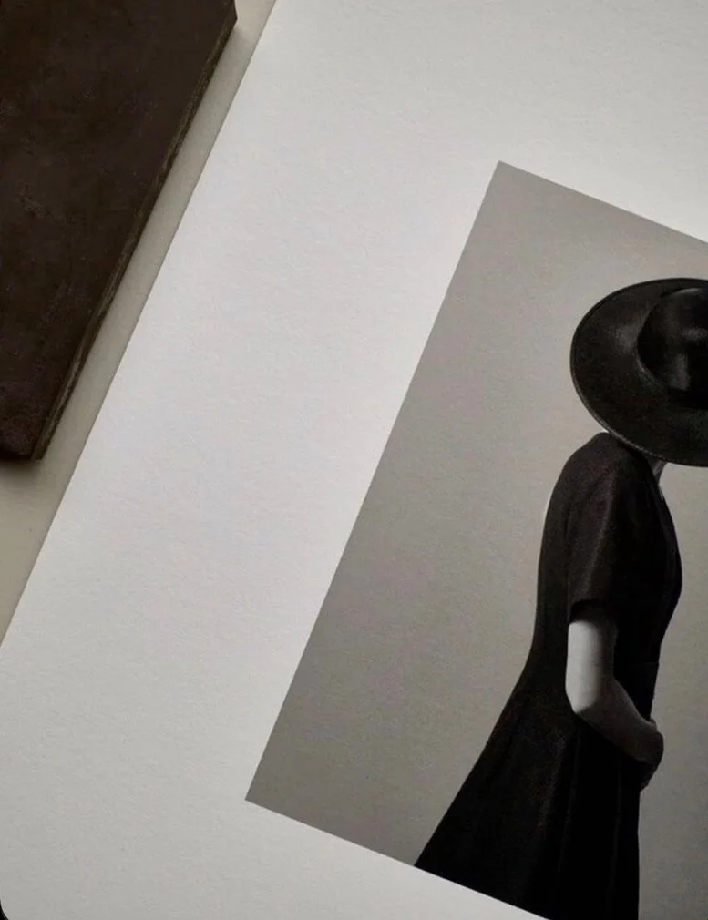 A black mannequin wearing a wide-brimmed hat and a dark dress, with a light background, partially visible in the image.