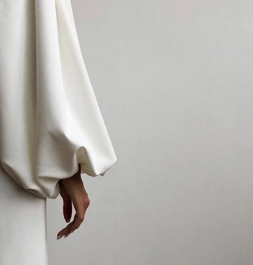 A person in a white long-sleeve shirt with a large cuff is hanging outside of a white door, with only their hand and part of their arm visible.