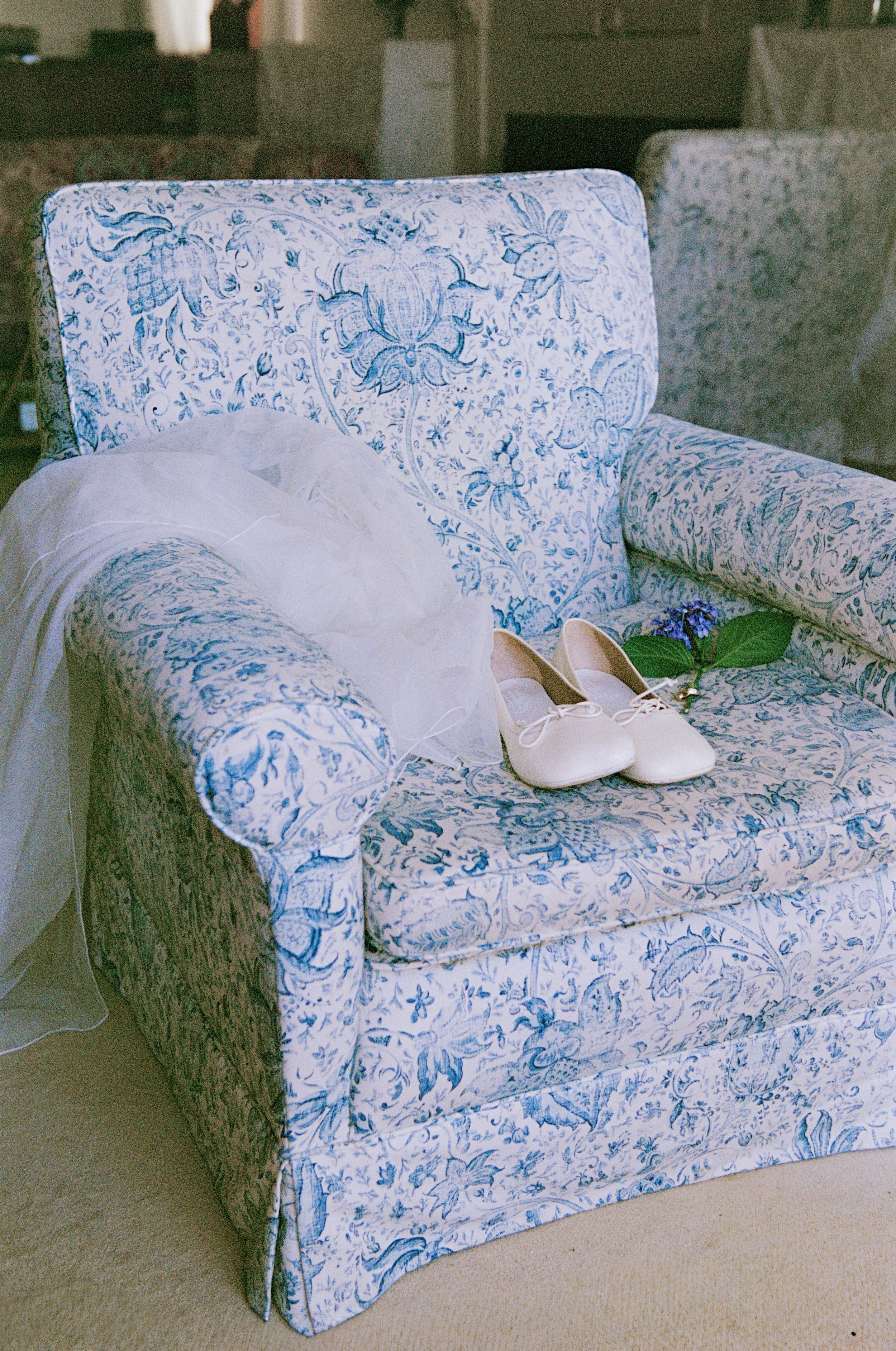 Wedding veil, white shoes, and a purple flower on a floral upholstered couch.