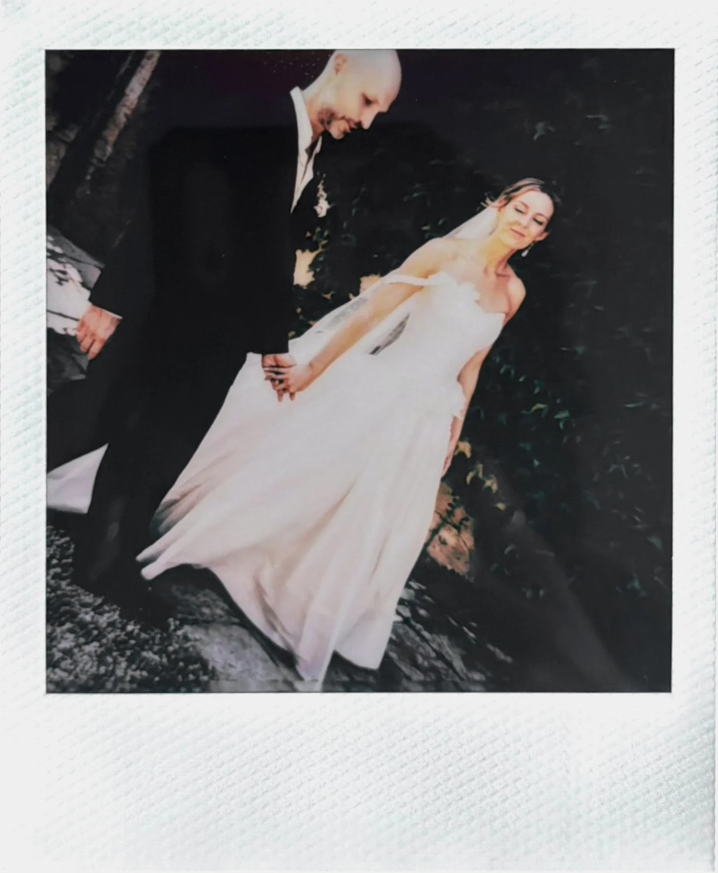 A bride and groom holding hands outdoors during their wedding, with the bride in a white wedding dress and veil, and the groom in a black tuxedo.