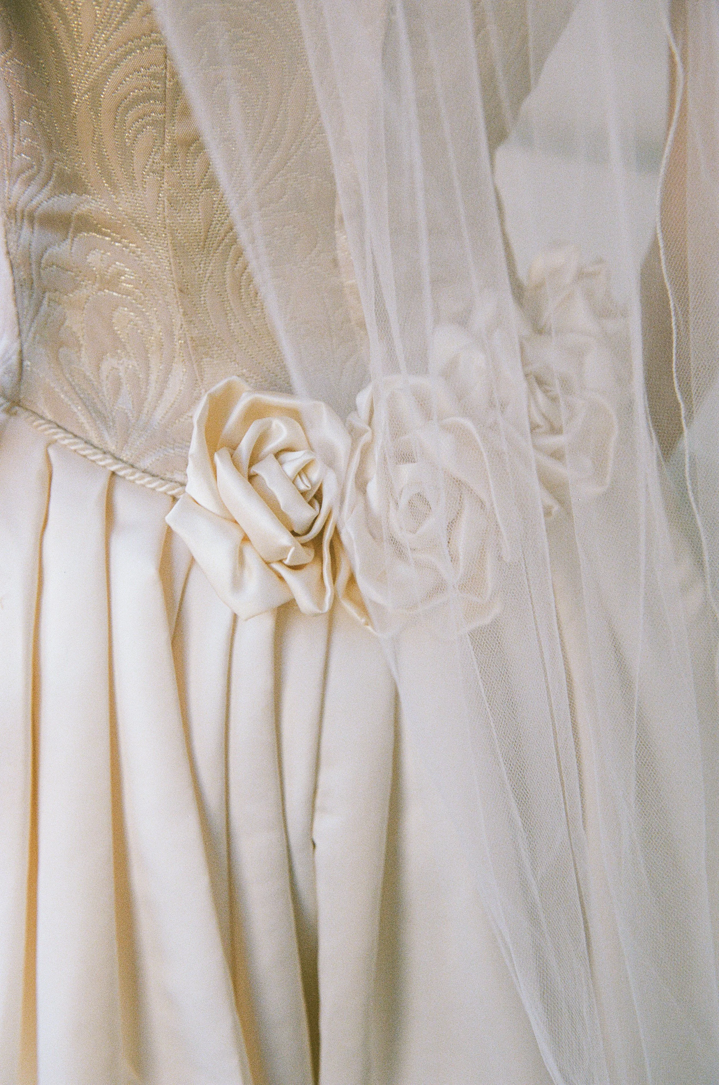 Close-up of a wedding dress with lace, satin fabric, and fabric roses decorative details.