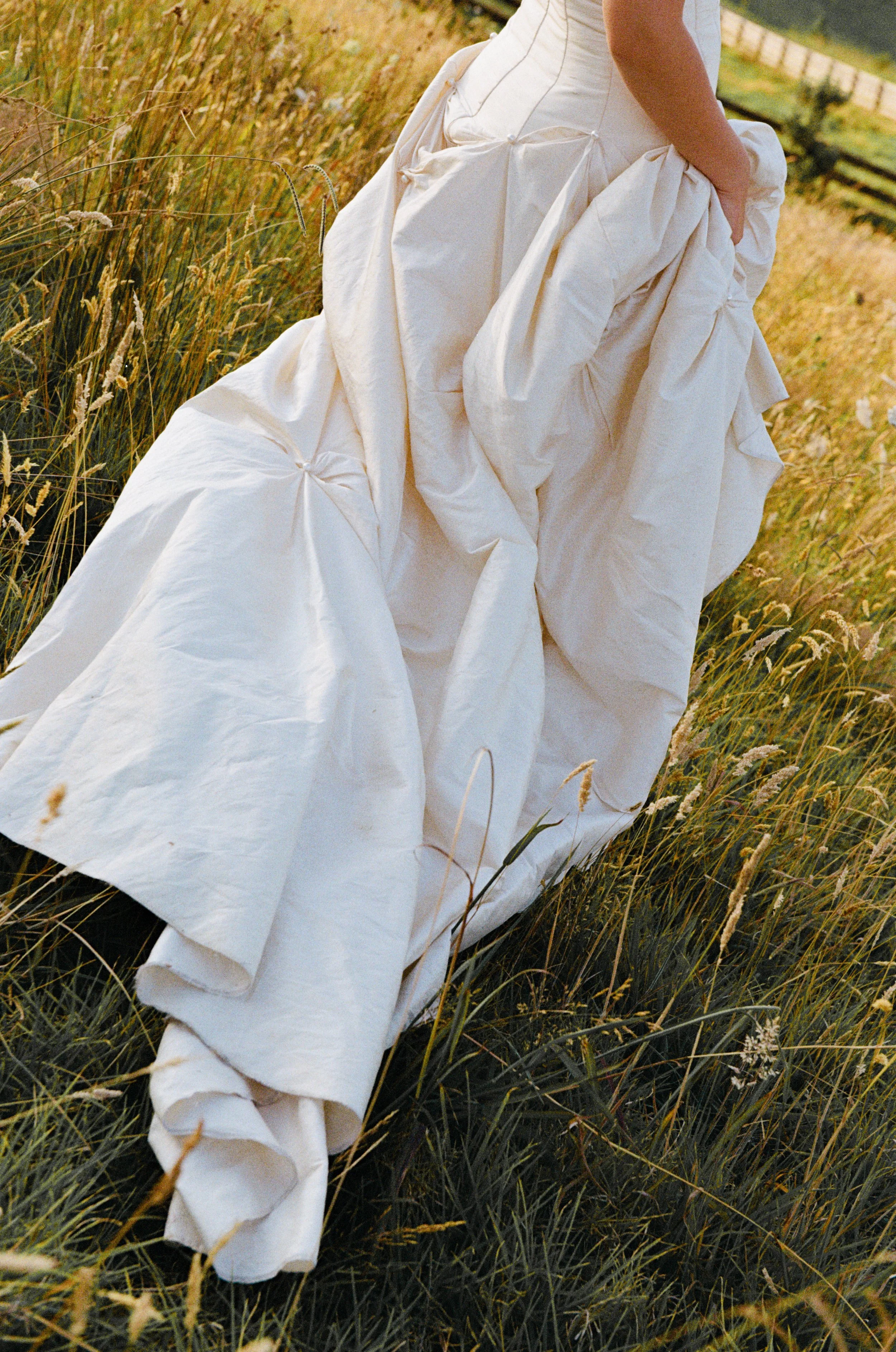 Close-up of a person in a white dress walking through a grassy field with tall wildflowers.