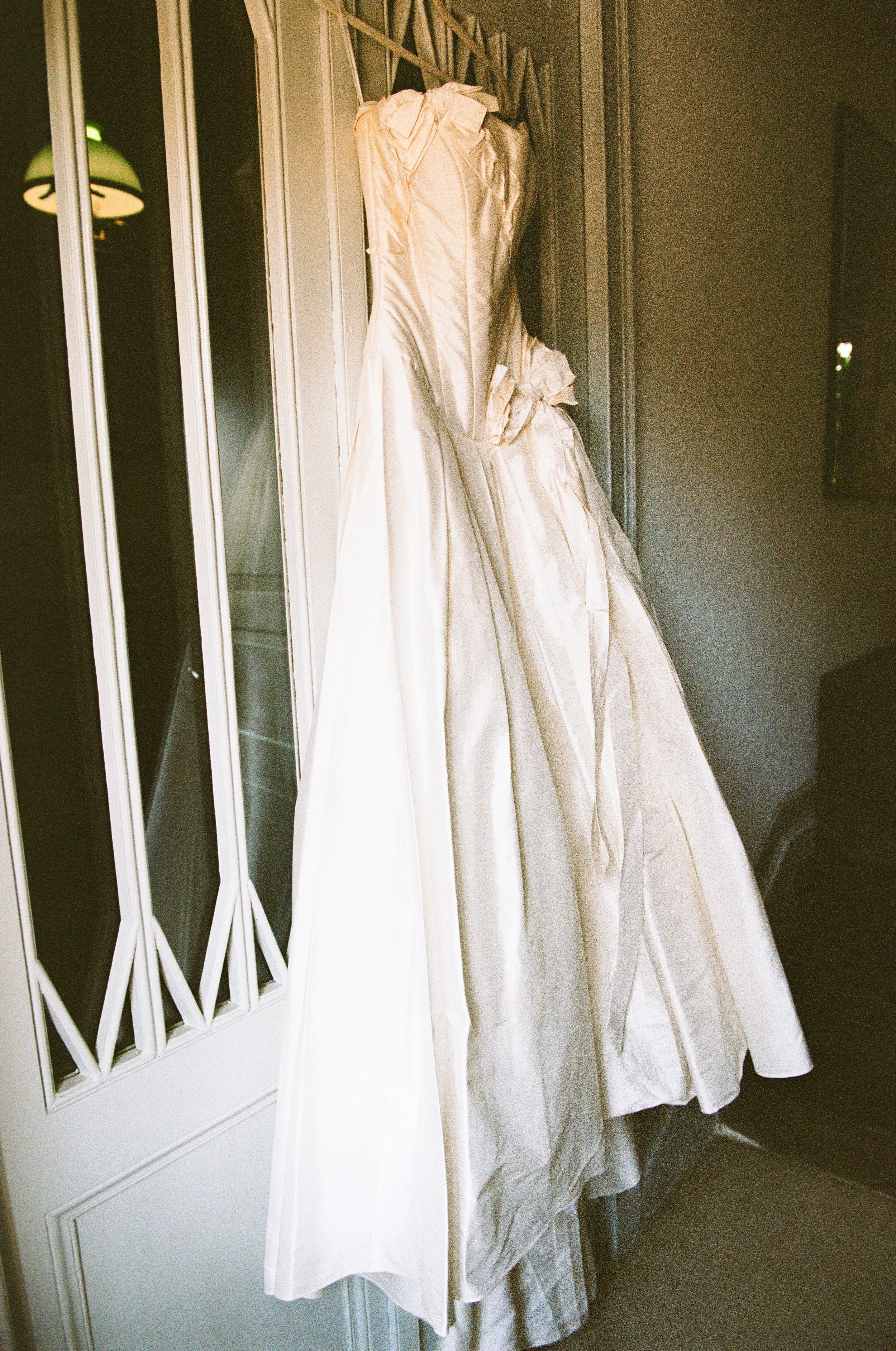 A wedding dress hangs on a hanger beside a glass-paneled door.